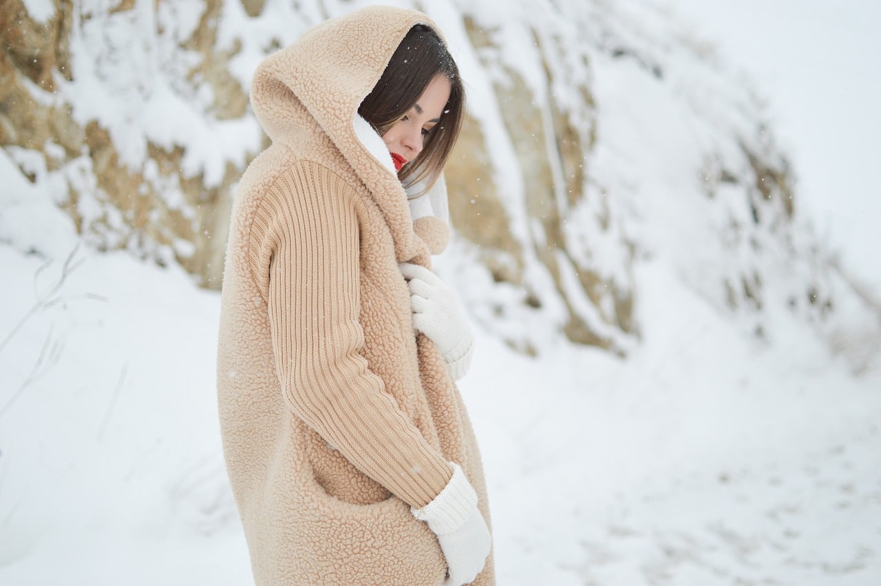 Femme dans la neige avec veste chaude et capuche, idéale pour parler de confort thermique et de grand froid.