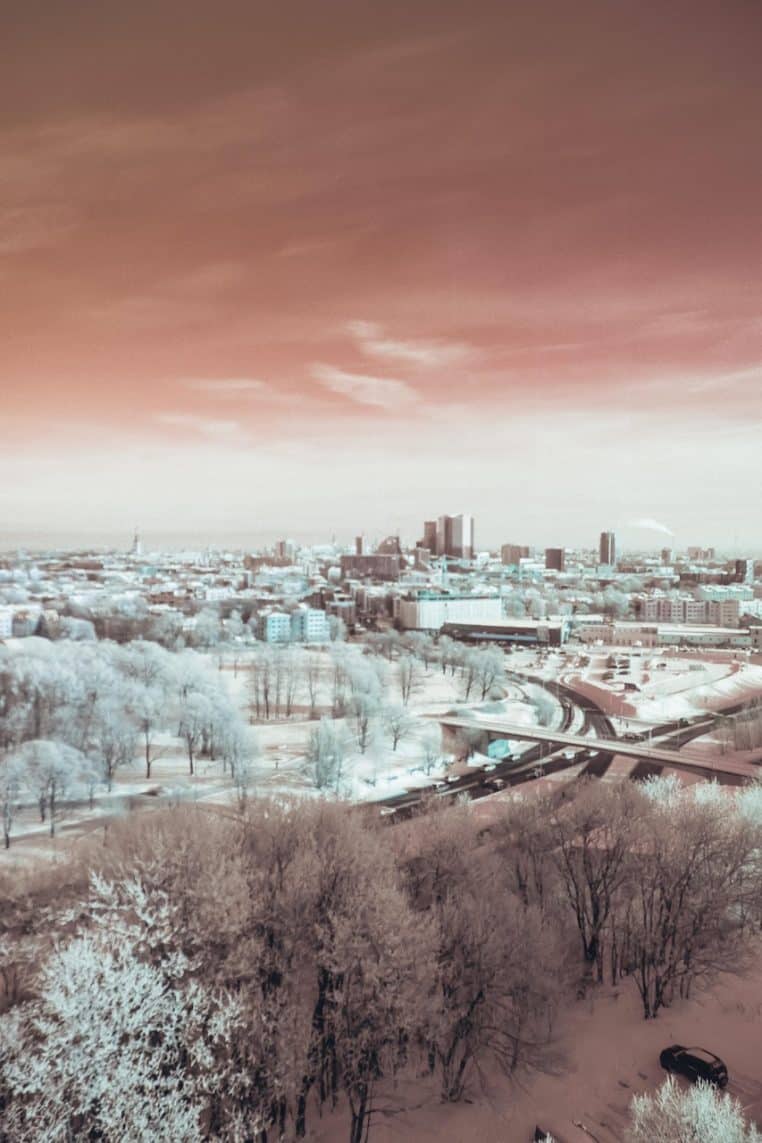 Panorama urbain avec gratte-ciel au loin, grands parcs recouverts de neige et ciel d’hiver rosé donnant une ambiance glaciale et irréelle.