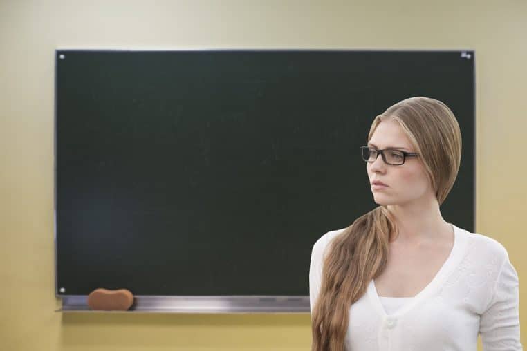 Prof debout devant un grand tableau noir, accueillant les élèves avec un message de bienvenue écrit à la craie.