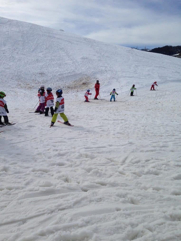 Enfants en combinaison colorée sur une piste de ski enneigée, skis aux pieds et casques bien ajustés