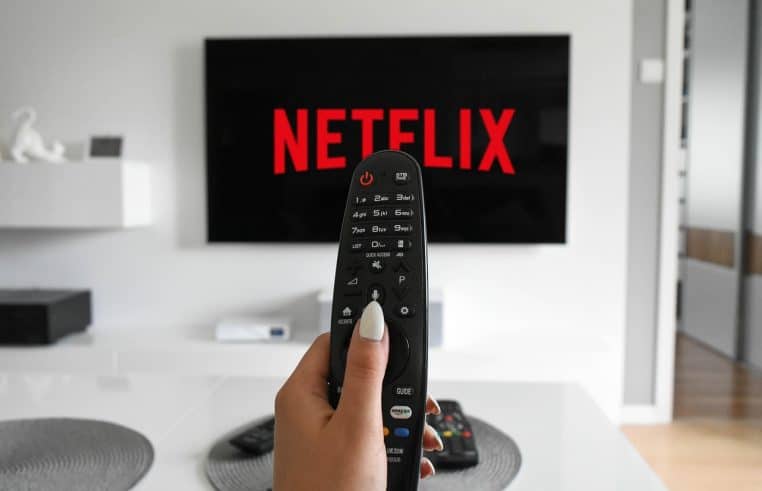 Main tenant une télécommande pointée vers un téléviseur affichant Netflix dans un salon moderne, illustrant la consommation de contenus en streaming.