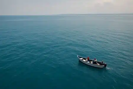 Petite barque de pêcheurs dérivant sur un vaste océan bleu au large du Panama, avec côte brumeuse et ciel pâle à l’horizon.