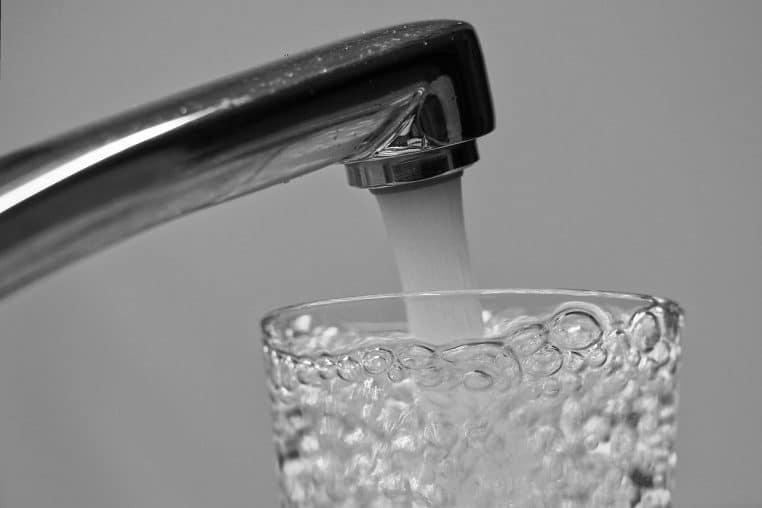 Jet d’eau puissant sortant d’un robinet métallique, avec éclaboussures figées en plein mouvement, symbole de la pression du réseau domestique.