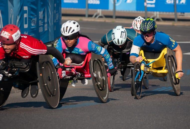 Athlètes en fauteuil roulant lancés à pleine vitesse lors d’une course sur route, dans le cadre d’une compétition de handisport en plein air.
