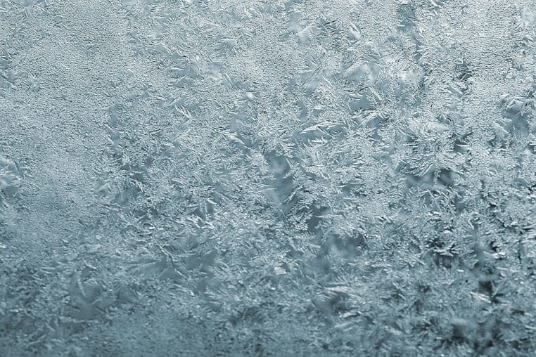 Gros plan sur une fenêtre givrée en plein hiver, motifs de glace couvrant la vitre d’un logement chauffé