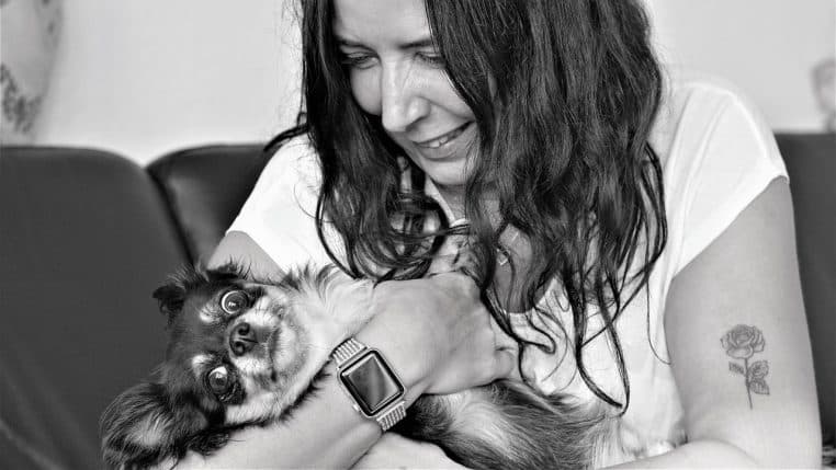 Femme souriante assise sur un canapé tenant un chihuahua contre elle, profitant d’un moment de proximité tendre avec son animal.