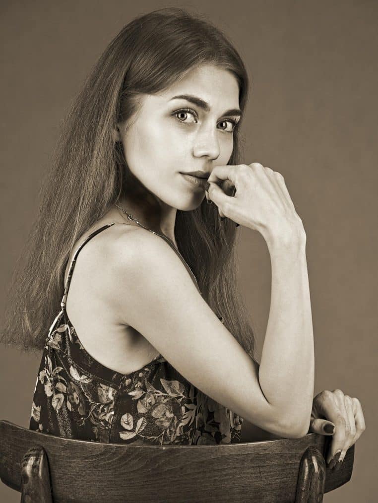 Femme assise, le regard lointain et fermé, semblant réfléchir intensément, pour évoquer les pensées négatives héritées des paroles blessantes de l’enfance.