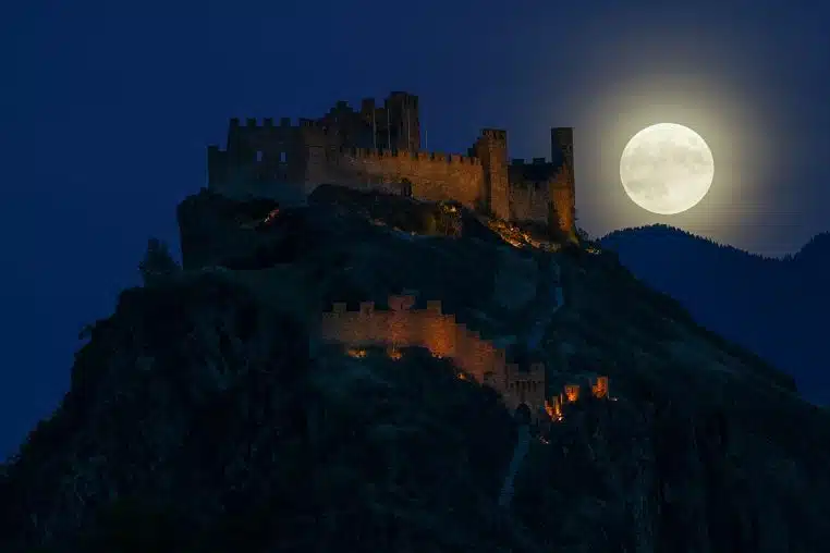 Pleine lune se levant derrière le château de Tourbillon, silhouette du relief suisse dans la nuit bleutée.