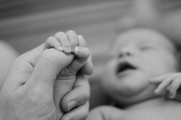 Gros plan d’un bébé tenant le doigt d’un parent, main adulte et main de nouveau-né en noir et blanc, très nette.