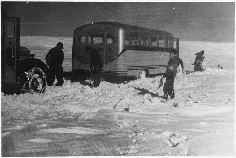Bus scolaire immobilisé dans la neige, des personnes dégagent la route dans un paysage d’hiver