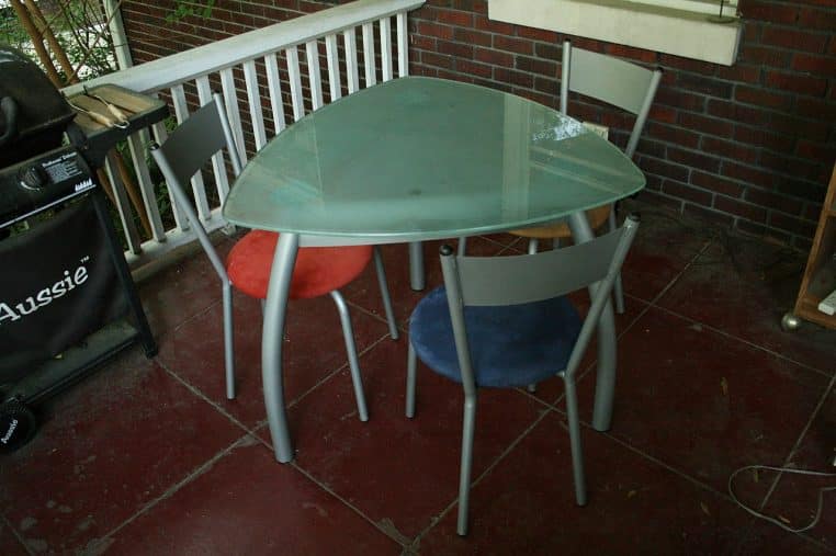 Table en verre sur une terrasse, entourée de chaises de couleurs différentes.