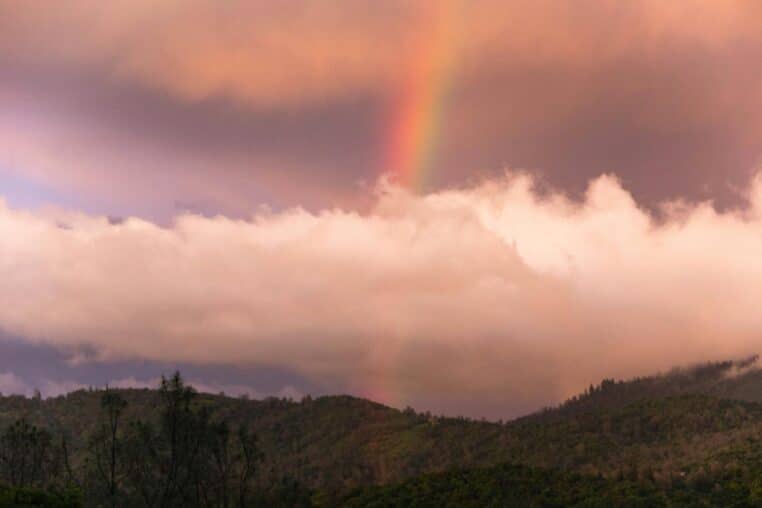 A beautiful rainbow arcs over the lush green mountains of Oroville, California at sunrise.