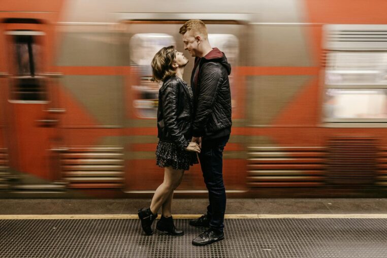 A couple embraces at a train station, symbolizing love amidst movement.