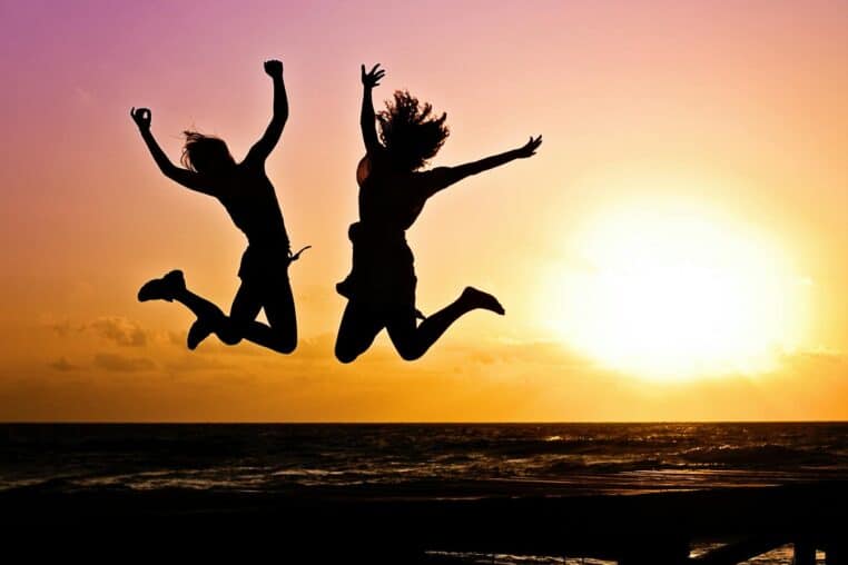 Silhouettes of two people joyfully jumping on a beach during a vibrant sunset.