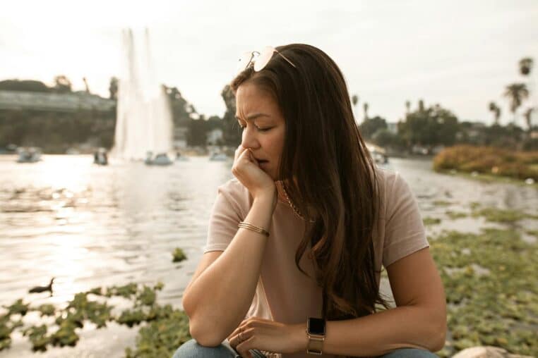 A thoughtful woman sits by a fountain, reflecting near a lake.