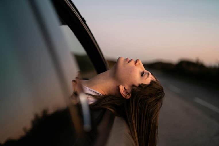 A woman leans out of a car window, enjoying a sunset drive on a quiet road.