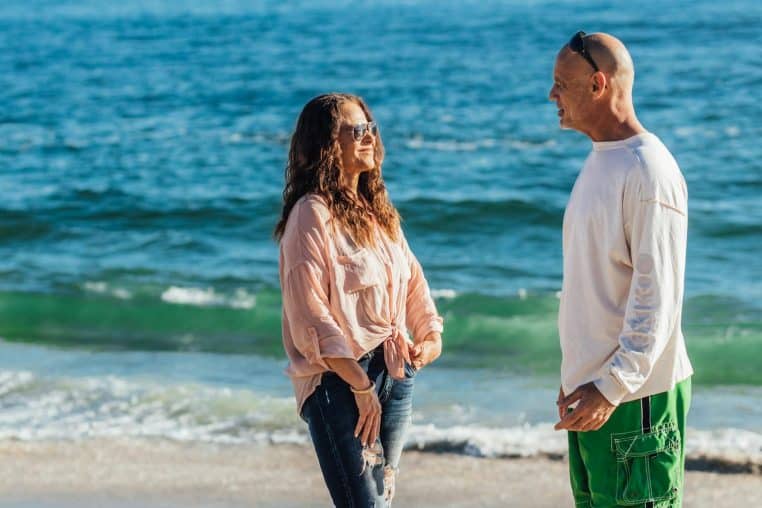 A couple enjoying a cheerful conversation on a sunny beach day, facing the ocean waves.