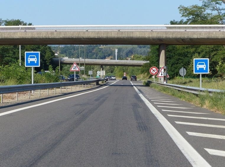 Chaussée d’autoroute avec nombreux panneaux et signalisation, circulation au loin sous un pont