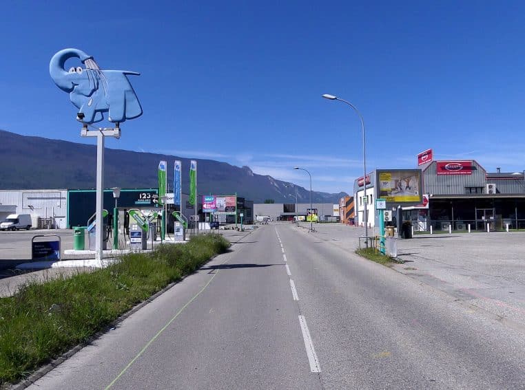 Allée de supermarché remplie de fruits et légumes, avec panneaux de prix et présentoirs sur plusieurs mètres.