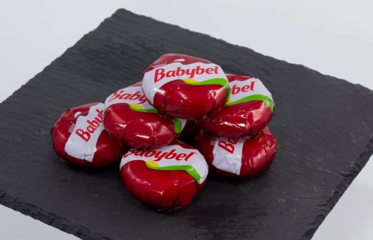 Mini Babybel posé sur une ardoise, cire rouge brillante et fromage blanc visible après ouverture partielle.