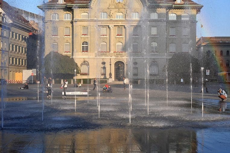 Jets d’eau sur la Bundesplatz à Berne, avec le bâtiment de la Banque nationale suisse en arrière-plan, en lumière douce