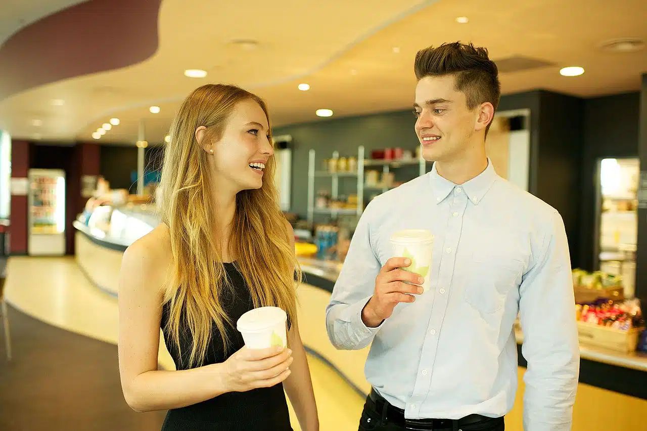 Un homme et une femme discutent dehors, devant un café, en souriant.