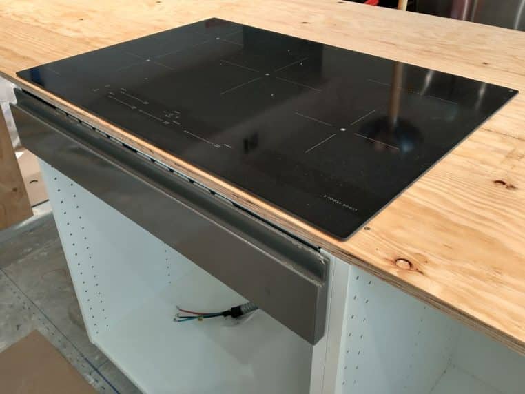 Table de cuisson noire posée sur un plan de travail en bois clair, avec repères discrets des zones de chauffe.