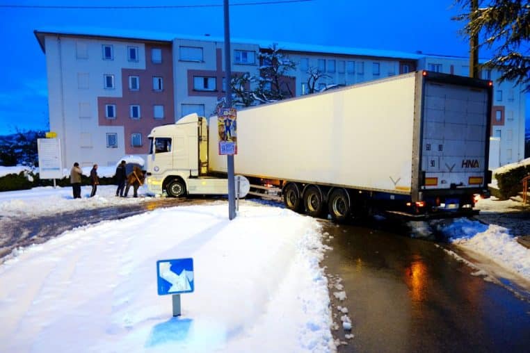 Camion semi-remorque bloqué sur une route enneigée, neige au sol et circulation ralentie en arrière-plan