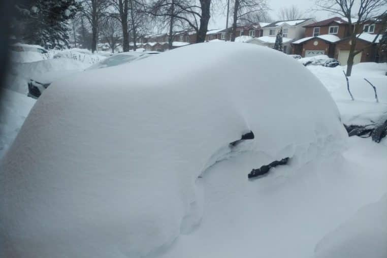 Voiture entièrement recouverte de neige après une tempête, stationnée dans une rue résidentielle en hiver