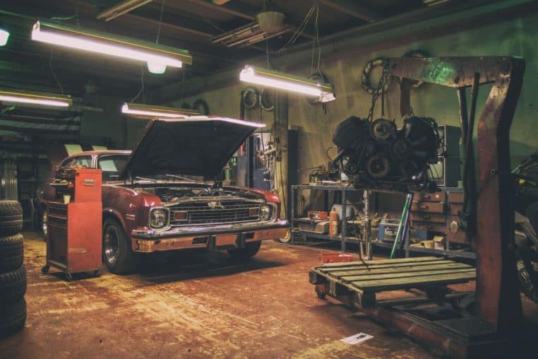 Vintage car repair shop with an old American car, engine hoist and tools inside a garage workshop
