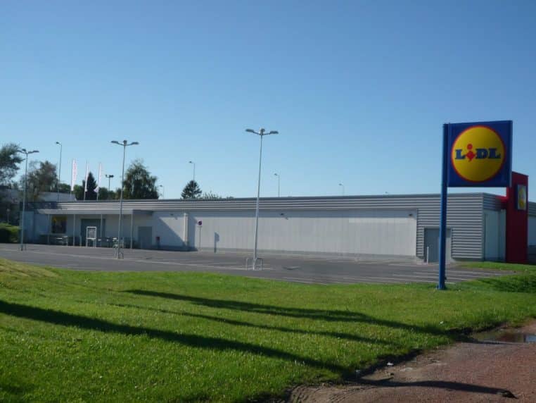 Bâtiment Lidl vu de loin avec grand logo sur mât, ciel bleu et vaste esplanade, photo horizontale.