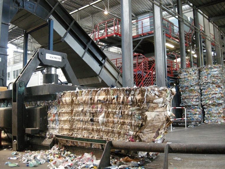 Intérieur d’un centre de tri avec convoyeurs et balles de déchets compactés, ambiance industrielle, vue large