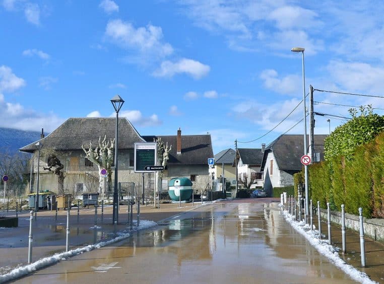 Rue à Chambéry-le-Vieux, neige fondante sur la chaussée, trottoirs mouillés et ciel dégagé d’hiver.