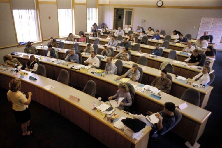 Salle de cours avec une formatrice face à des adultes en formation, prise de vue en hauteur, ambiance studieuse.