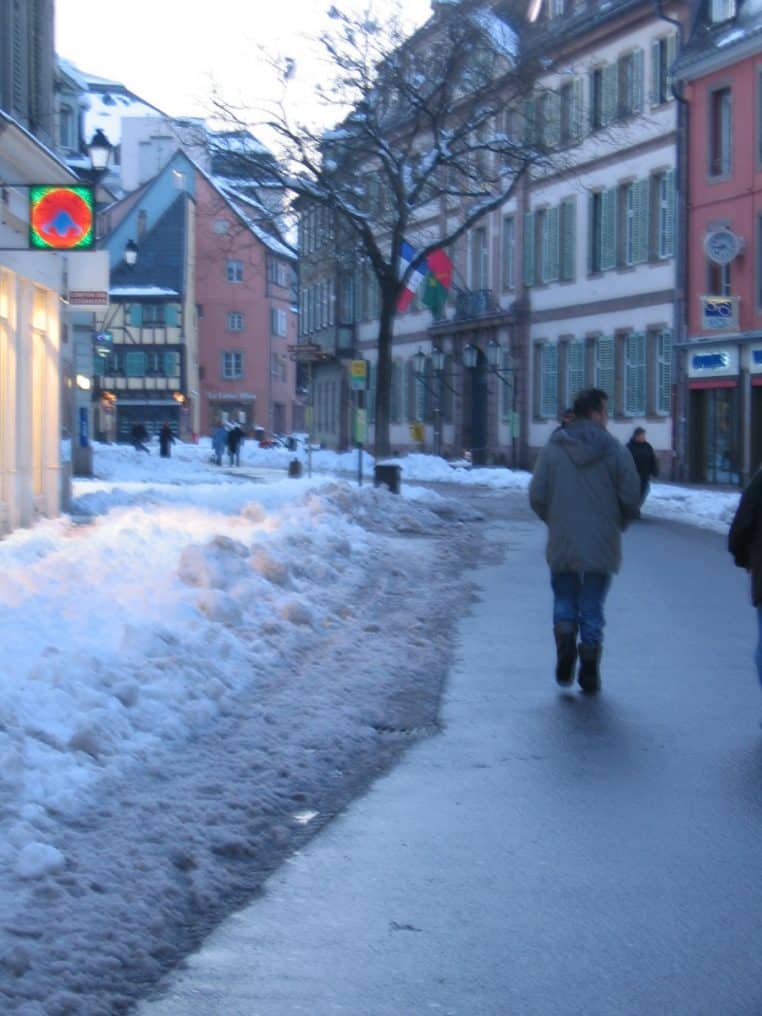 Rue de Colmar sous une épaisse couche de neige, avec des façades d’immeubles en arrière-plan.
