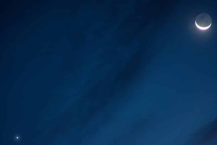 Conjonction entre Vénus et un fin croissant de Lune, visibles dans un ciel bleu profond au petit matin.