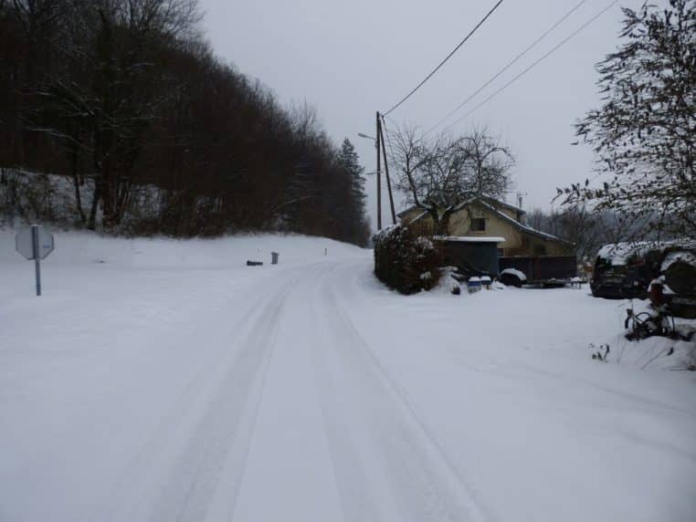 Route départementale enneigée en France, marquages visibles, accotements blancs et circulation prudente en hiver