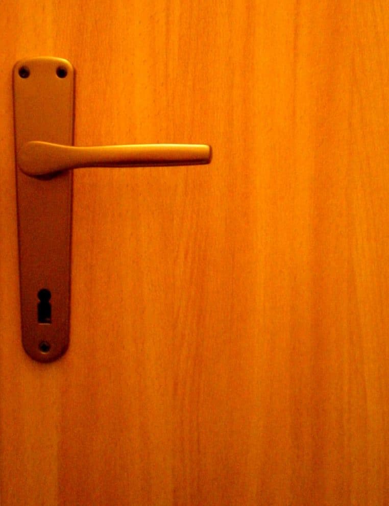 Main ouvrant une porte via une poignée métallique.