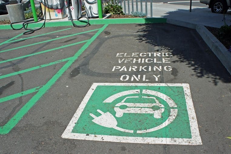 Borne de recharge en ville près d’une zone touristique, stationnement et signalisation dédiés aux voitures électriques.