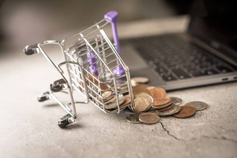 Mini chariot de courses renversé près d’un ordinateur portable, pièces éparpillées, idée d’achat impulsif.