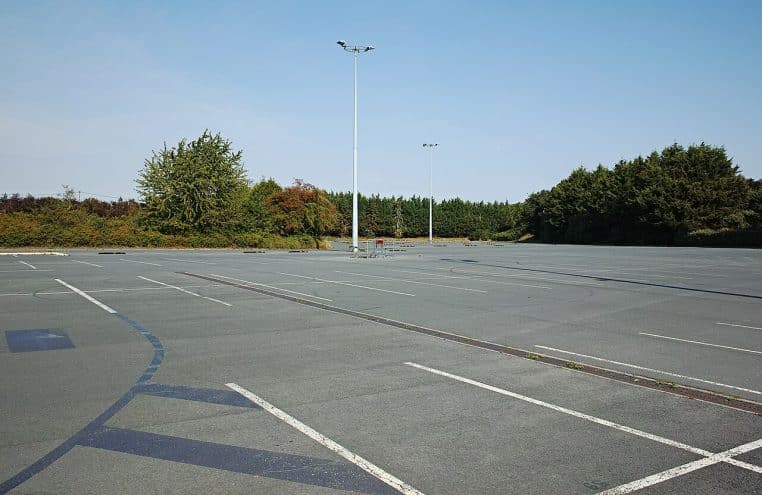 Parking d’un supermarché avec rangées de voitures, marquage au sol et allées de circulation