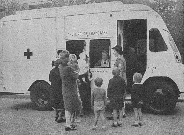 Véhicule de la Croix-Rouge française et personnes rassemblées, photo d’archive en noir et blanc, paysage.