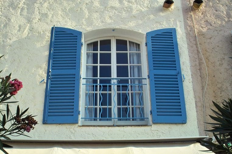 Fenêtre avec volets battants bleus sur une façade claire.