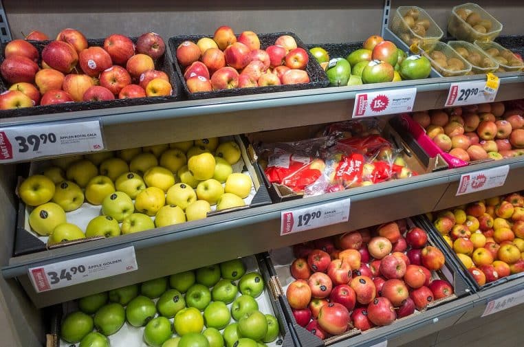 Étal de fruits et légumes dans une épicerie, avec cagettes alignées et étiquettes de prix.