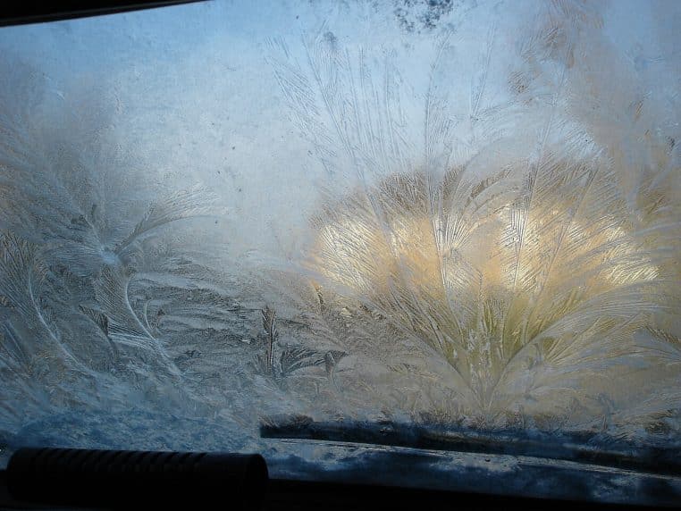 Motifs de givre sur un pare-brise vus de l’intérieur, avec la lumière du matin qui traverse les cristaux gelés.