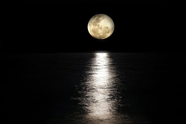 Pleine lune au-dessus de la mer sombre, reflet lumineux vertical sur l’eau, horizon net dans la nuit noire.