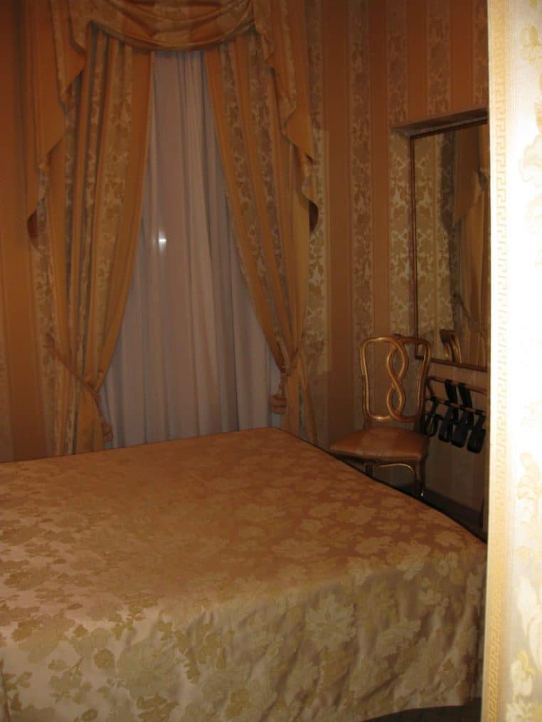 Intérieur d’une chambre d’hôtel avec lit et rideaux, vue en perspective, ambiance chaude et intimiste.