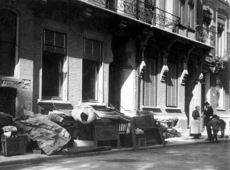 Meubles et cartons sur un trottoir après une expulsion, scène urbaine prise en extérieur, grand angle.