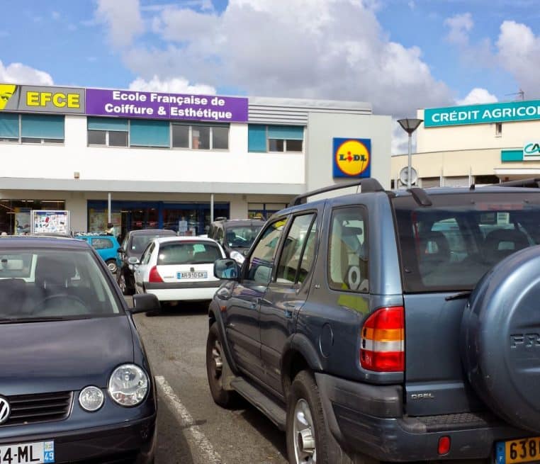 Façade d’un magasin Lidl en France avec parking rempli, enseigne visible et ciel lumineux en arrière-plan.