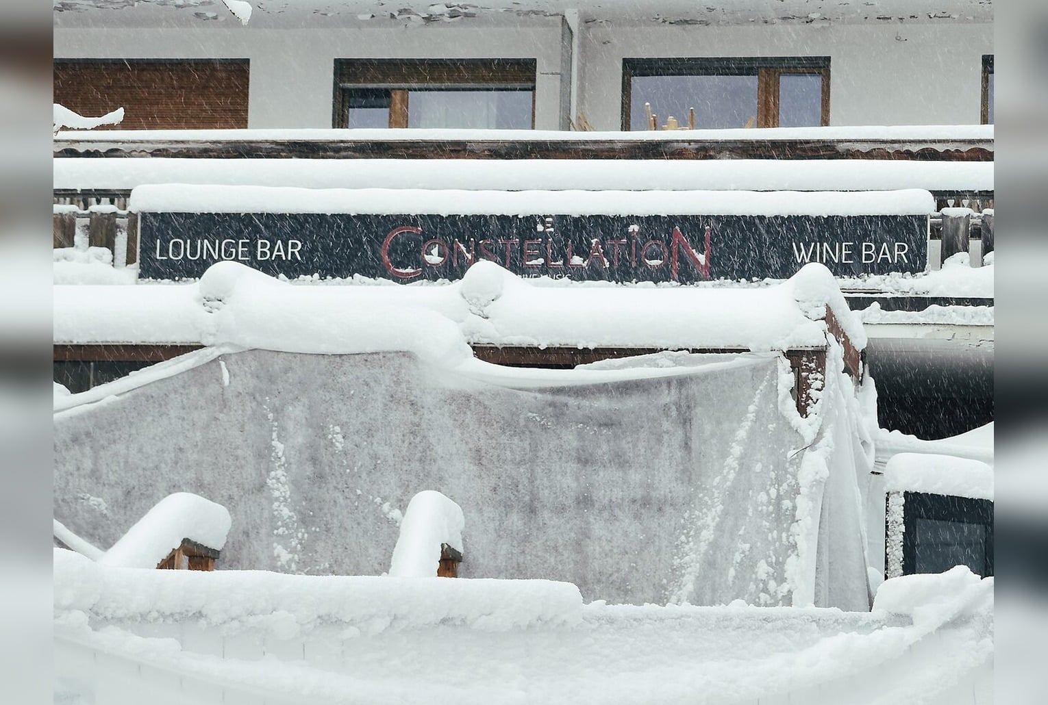 Façade enneigée du bar « Le Constellation » à Crans-Montana, prise de jour, sans scène choquante.